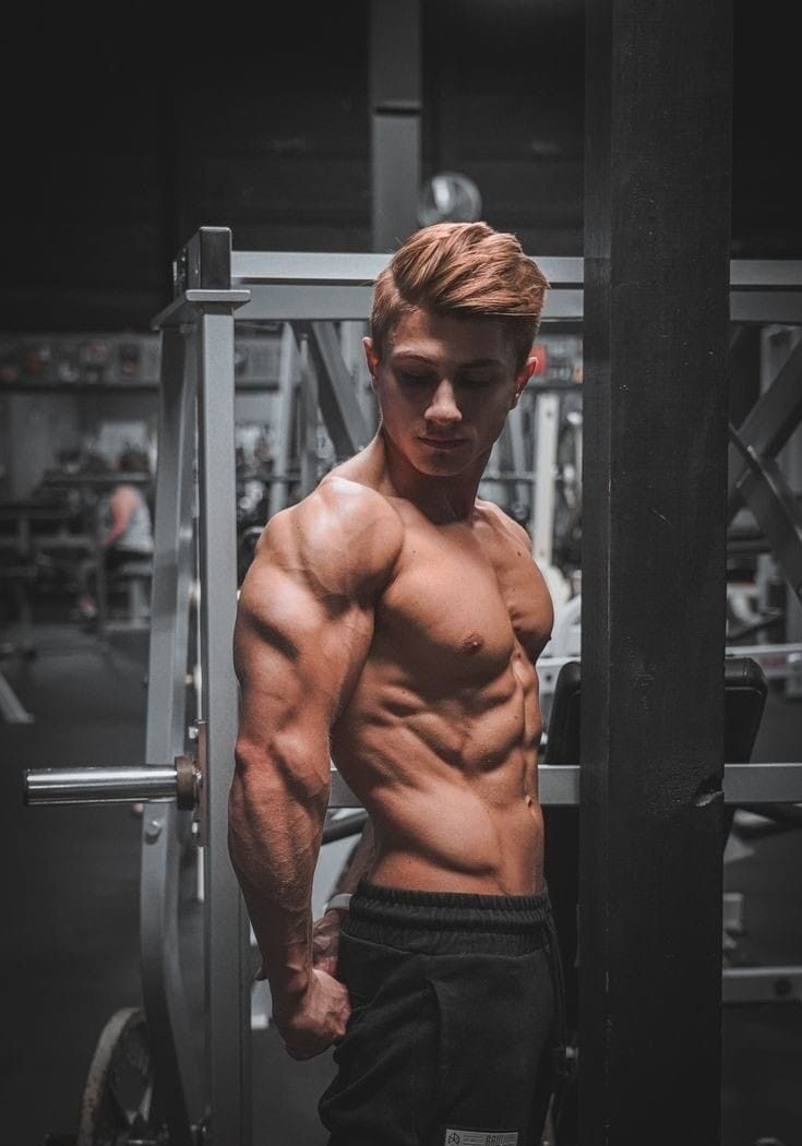 Muscular young man posing in gym setting, showcasing physique and strength, relevant to discussions on muscle growth and fitness supplements.