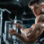 Muscular man holding syringe in gym illustrating anabolic steroid use and Mast Propionate cycle.